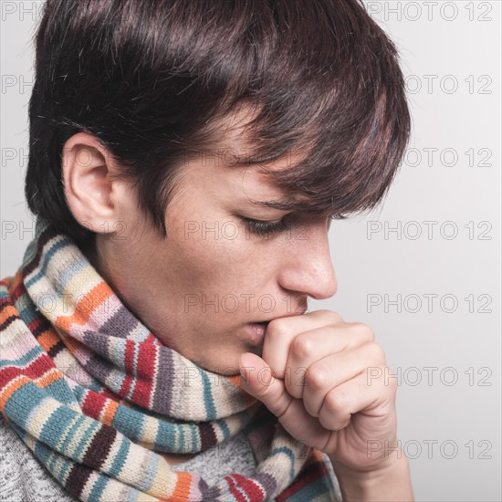 Woman wearing multicolored scarf around neck coughing against gray backdrop