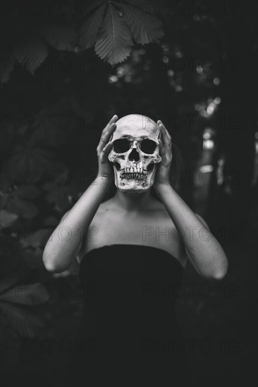 Woman holding human skull forest