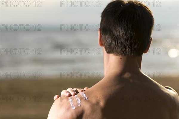 Back view man applying sunscreen lotion
