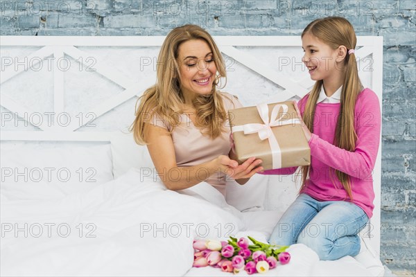 Daughter giving gift box mother bed