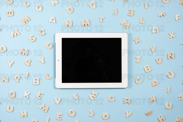 Digital tablet with black screen display surrounded with wooden letters blue background