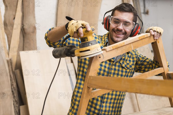 Skilled carpenter is using power sander as tool polish his furniture