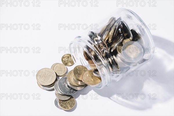 Spilled out coins from glass container white background