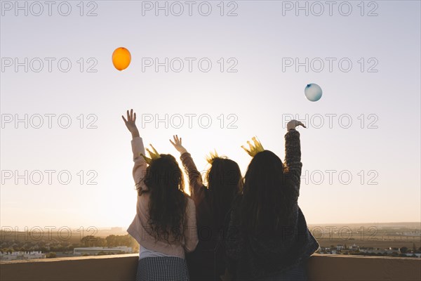 Back view girls throwing balloons from roof