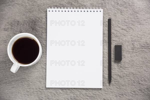 Elevated view coffee cup blank spiral notepad with black eraser pencil gray desk