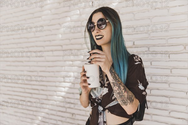 Modern beautiful young woman wearing sunglasses holding disposable coffee cup