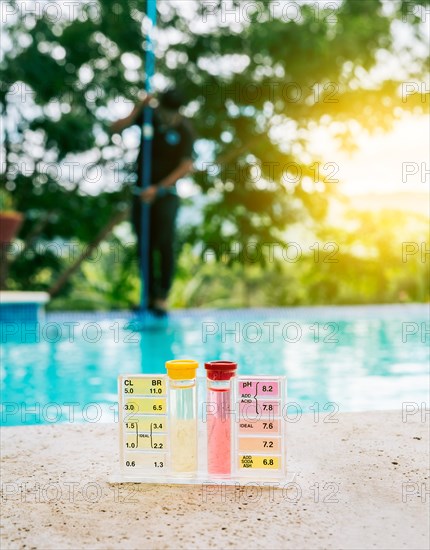 Water PH tester kit on the edge of the swimming pool with maintenance person in the background
