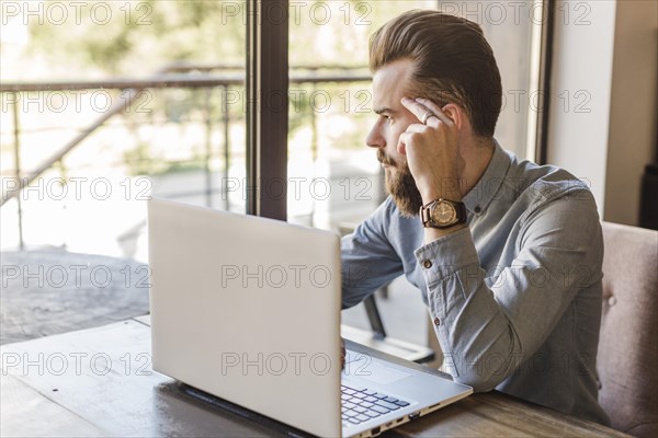 Man looking outside window with laptop desk caf