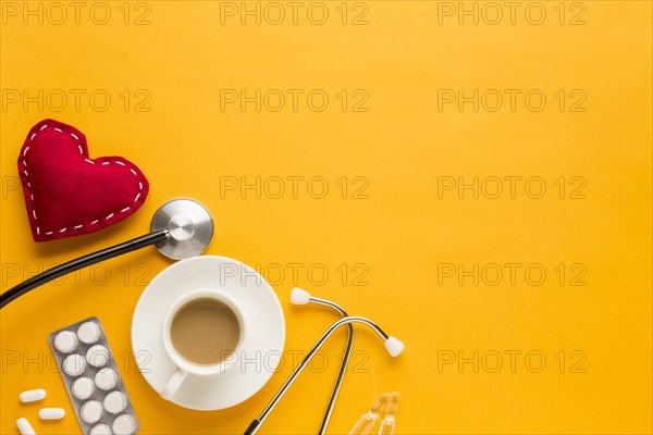 Coffee cup blister packed tablets stethoscope stitched heart shape against yellow background