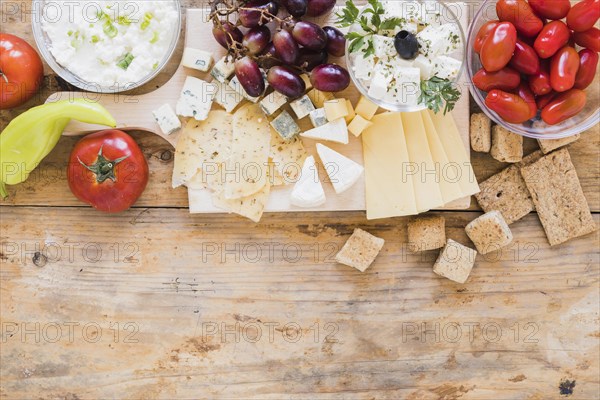 Green chilies pepper tomatoes grapes crisp bread cheese cubes desk