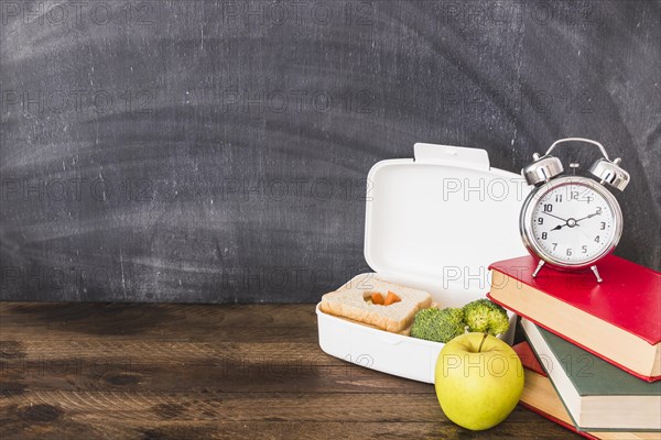 Lunchbox apple near books alarm clock