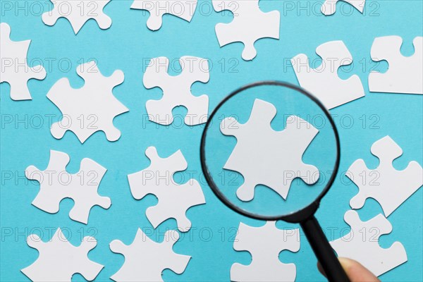 White jigsaw piece seen through magnifying glass blue white background