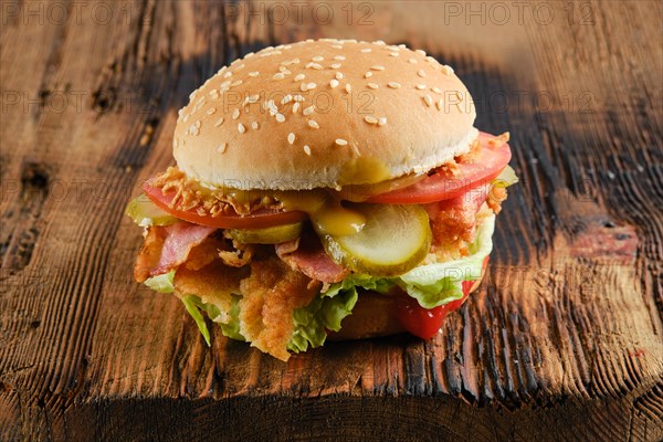 Kentucky chicken burger with pickled cucumber and fresh tomato on wooden background