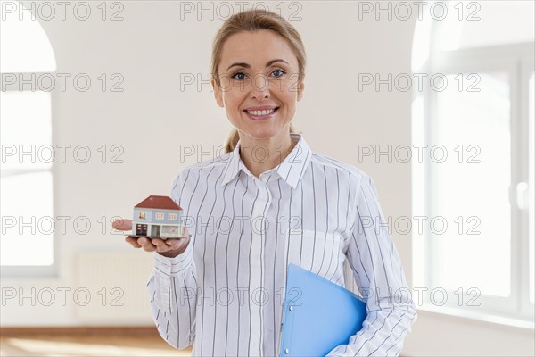 Front view smiley female realtor holding miniature house