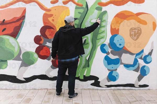 Rear view man making graffiti with spray can wall