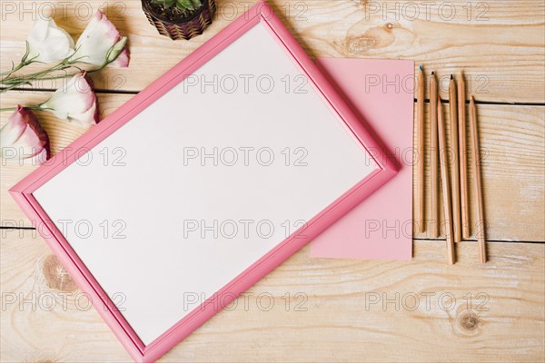 Colored pencils paper eustoma flowers white picture frame with pink border wooden table