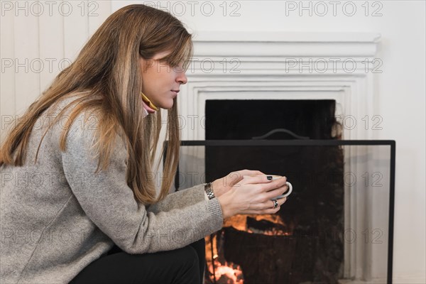 Woman sweater drinking tea near fireplace