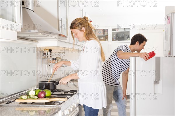 Smiling woman cooking vegetables while her husband opening refrigerator door