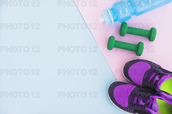 Water bottle sport shoes dumbbells pink backdrop blue background
