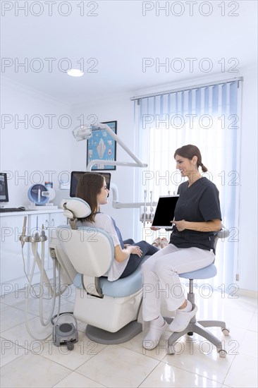 Female dentist pointing digital tablet screen patient sitting chair clinic