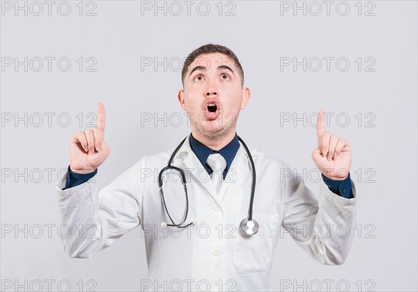 Amazed doctor pointing a promotion up. Male doctor looking and pointing up isolated