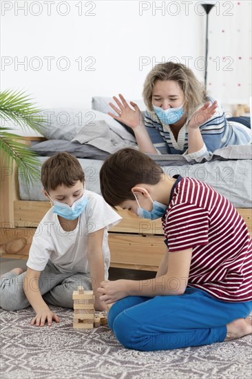 Children with medical masks playing jenga home with mother