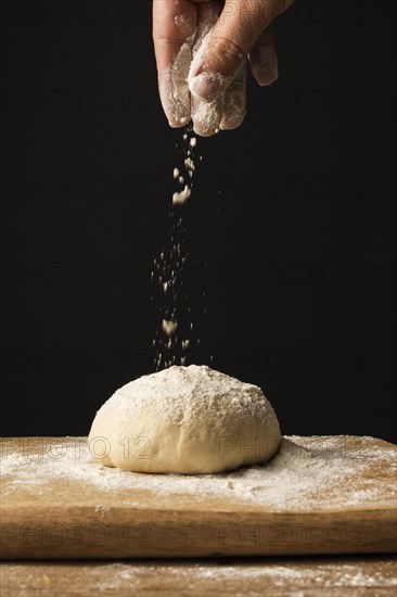 Front view hand sprinkling flour dough cutting board