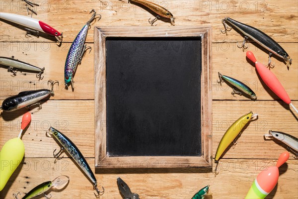 Different type fishing lures around black wooden slate wooden backdrop