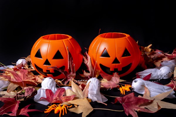 Halloween pumpkins on red autumn leaves and ghosts on a black background