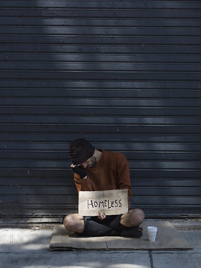 Homeless man hiding his face asking money long view