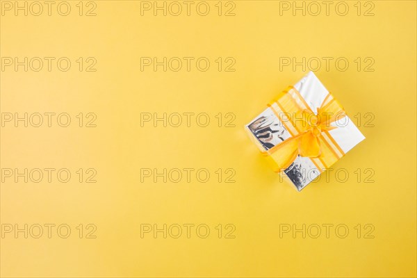 Silver gift box decorated with yellow ribbon yellow background