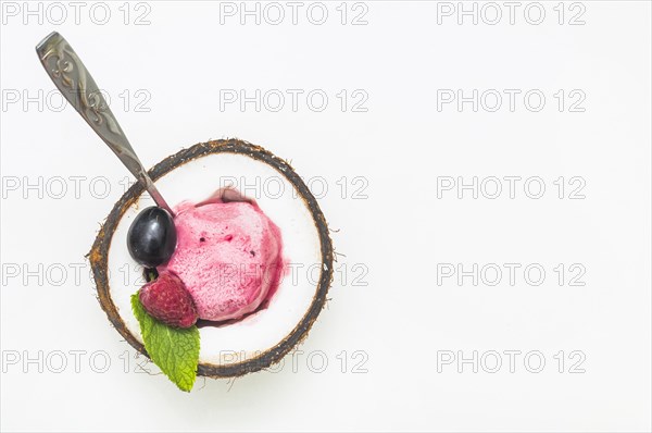 Raspberry ice cream inside halved coconut with spoon against white background