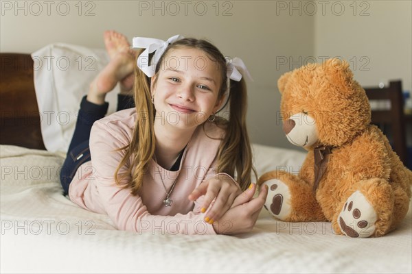 Smiling young woman lying bed with teddy bear