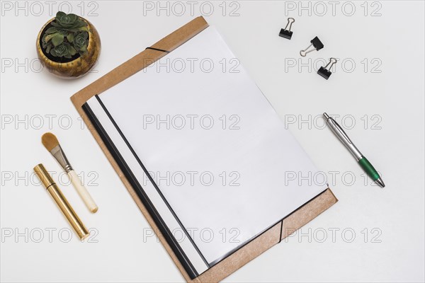 Blank spiral notebook with make up brush mascara paper clips pen with potted plant white desk
