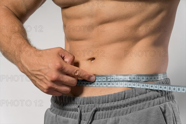 Fit man holding measuring tape around waist