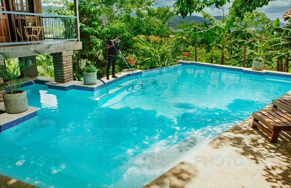 Man cleaning a beautiful swimming pool with suction hose. Pool maintenance and cleaning with vacuum hose. Swimming pool cleaning and maintenance service