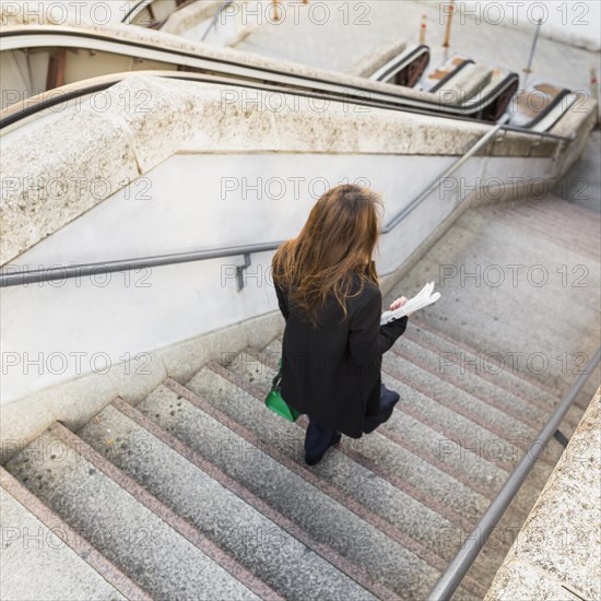 Business woman with newspaper walking down stairs