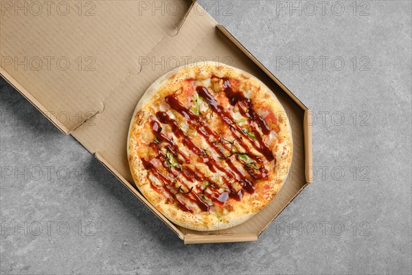 Top view of barbecue pizza with bacon and spring onion in cardboard box