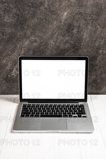 Laptop with blank white screen white wooden table against concrete