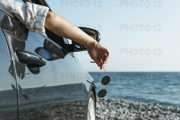 Mid shot woman hand hanging out car window near sea