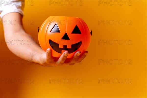 Hand holding an orange Halloween pumpkin on a background of yellow