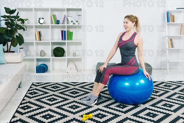 Portrait smiling fitness young woman sitting blue pilates ball looking away