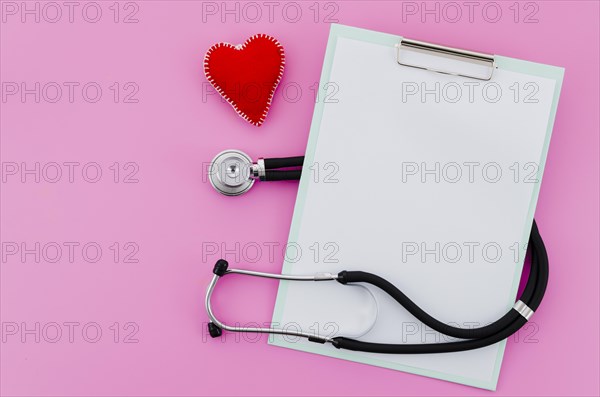 Elevated view hand made red heart with stethoscope clipboard pink background