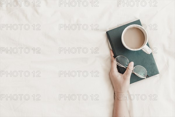 Woman s hand holding book with eyeglasses hot drink it