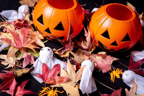 Detail of Halloween pumpkins over red autumn leaves and ghosts on a black background