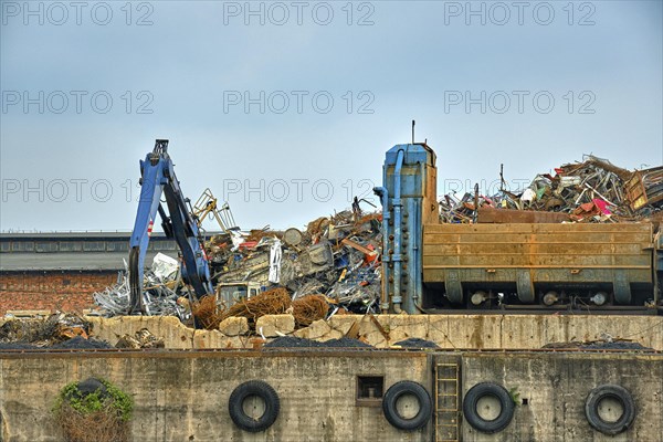 Old gantry crane and backhoe loader working over construction debris in river port in overcast day. Cloudy industrial image