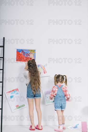 Little girls hanging drawings white wall