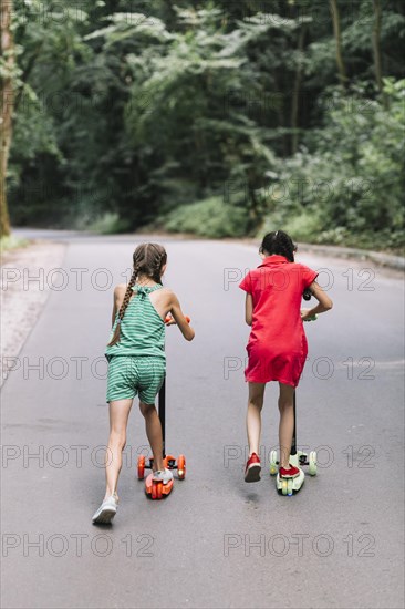 Rear view girl riding push scooters road