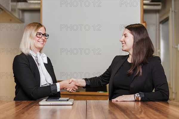 Women sitting table shaking hands smiling