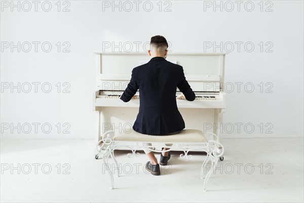 Rear view man playing piano sitting against white wall